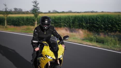 Un-Hombre-Vestido-De-Negro-Pasa-Conduciendo-Una-Moto-Deportiva-BMW-Amarilla-En-Una-Carretera-Asfaltada.