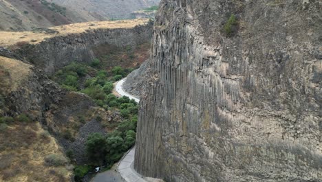 Flyover-of-ancient-basalt-cliff-tourist-site,-Garni-Gorge-in-Armenia