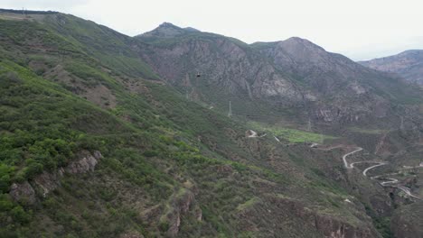 Aerial:-Tatev-cable-car-in-canyon-sky-in-front-of-switchback-mtn-road