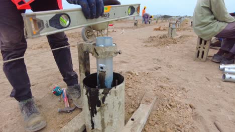 Construction-worker's-hands-installing-and-leveling-concrete-pile-frame-mould-and-support-for-solar-PV-concrete-pile---close-up-view,-Gambia