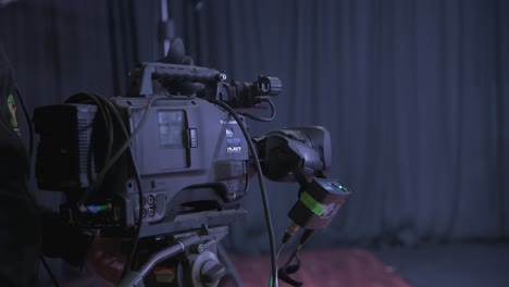 A-close-up-view-behind-a-camera:-an-operator-is-setting-up-a-camera-to-shoot-a-talk-between-5-men-in-suits-seated-in-modern-chairs