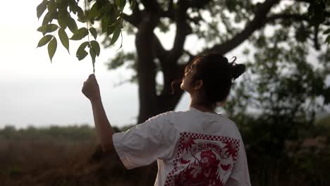 Young-woman-reaching-for-leaves-in-a-serene-outdoor-setting-during-golden-hour