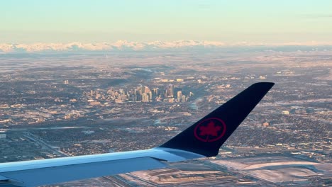 Mirando-Por-La-Ventana-Del-Avión-En-El-Ala-Del-Avión-Con-El-Logotipo-De-Air-Canada,-Con-Vistas-A-La-Ciudad-De-Calgary-Y-Las-Montañas-Rocosas.