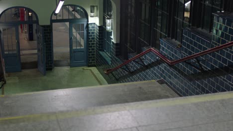 Nighttime-view-of-a-tiled-subway-entrance-with-blue-doors-and-vibrant-lighting,-stairs-leading-to-a-platform