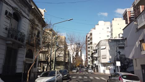 Establishing-shot-of-city-streets-in-autumn-daylight,-traditional-neighborhood-buildings-and-pedestrians-passing-by-quiet-road-with-cars,-motorcycles-and-bicycles