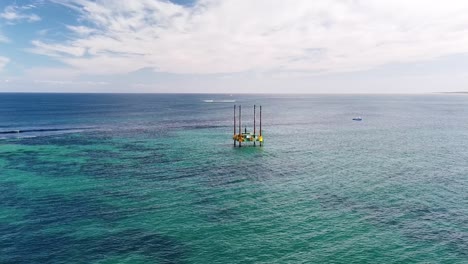 Descending-aerial-view-of-geological-drilling-platform-working-in-shallow-waters-near-Alkimos-Reef,-Perth