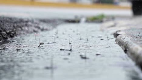 Close-up-rainfall-on-a-ditch-in-the-street,-car-drives-by,-slowmotion