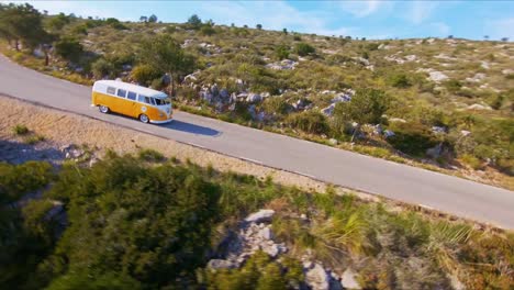 FPV-drone-flying-around-a-camper-van-driving-along-a-lonely,-country-highway