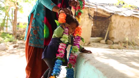 Indian-woman-puts-typical-flower-necklace-around-neck-of-adorable-baby-girl-in-Noondpura-village,-Rajasthan