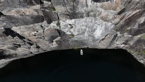 Drone-captures-a-rib-boat-near-a-towering-mountain-wall-in-a-Norway-fjord,-offering-dramatic-aerial-perspectives