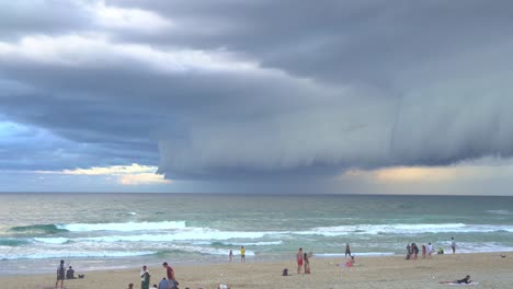 People-gathered-at-Surfers-Paradise-beach,-Gold-Coast,-observing-a-dramatic-apocalyptic-scene-unfolding-in-the-sky,-with-thick-layers-of-ominous-clouds-sweeping-across-the-horizon