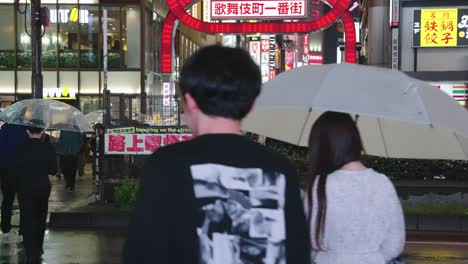 Slow-motion-pan-as-Japanese-people-cross-road-at-night,-into-night-life-central-area-in-Japan