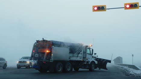 Snow-plow-truck-with-flashing-lights-passing-through-street-lights-at-intersection