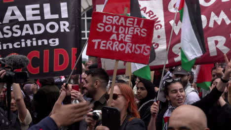 A-person-holds-a-red-placard-that-reads,-“Israeli-soldiers-are-terrorists”-as-people-make-the-peace-sign-hand-gesture-during-a-Nakba-day-protest-march