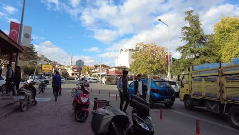 On-a-sunny-day,-a-yellow-van-is-driving,-and-people-shop-and-walk-in-a-local-street-in-Avanos-city-in-Cappadocia-Turkey