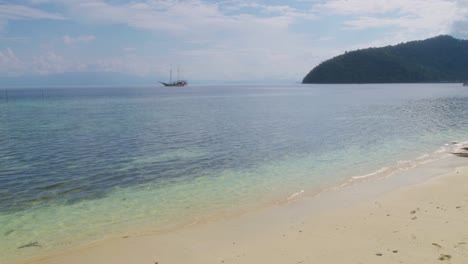 Las-Prístinas-Costas-De-La-Isla-Kri-En-Raja-Ampat,-Indonesia,-Con-Aguas-Cristalinas-De-Color-Turquesa-Y-Un-Velero-Anclado-En-La-Distancia.