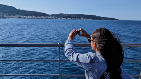 Una-Joven-Morena-Con-El-Pelo-Volando-Al-Viento-Y-Gafas-Filma-El-Mar-Azul