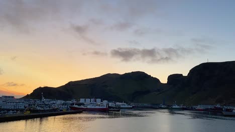 Fischerboote-Angedockt-Im-Hafen-Von-Vestmannaeyjar-Bei-Sonnenuntergang-Mit-Klippen-Im-Hintergrund