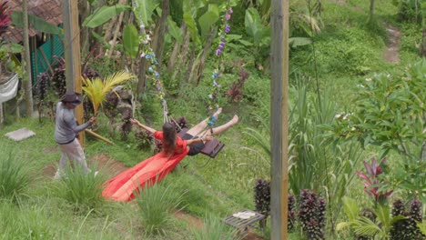 In-the-picturesque-rice-terraces-of-Tegallalang,-Bali,-Indonesia,-a-woman-swings-with-delight,-surrounded-by-lush-greenery