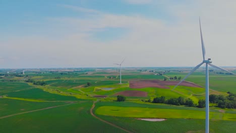 Sensational-shades-of-green-grass-beneath-rotating-wind-turbines-in-rural-countryside-field-on-sunny-day,-forward-aerial