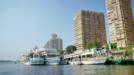 Cruise-boats-mooring-along-shore-with-apartment-block-buildings,-Cairo