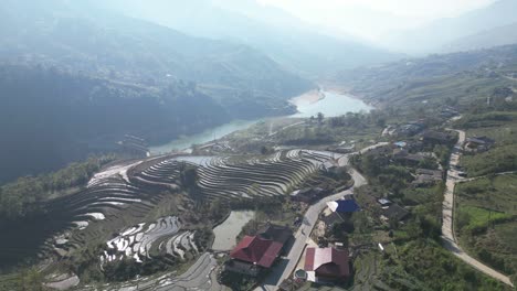 Aerial-drone-shot-of-villages-amidst-bright-green-rice-terraces-in-the-mountains-of-Sapa,-Vietnam