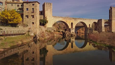 Medieval-stone-buildings-and-bridge-reflected-in-river-in-Besalu,-Girona,-Spain