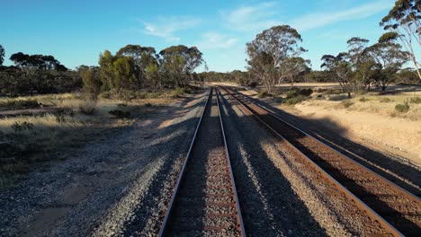 Aerial-flight-over-train-rails-in-sandy-woodland-terrain-of-Australia-at-sunset