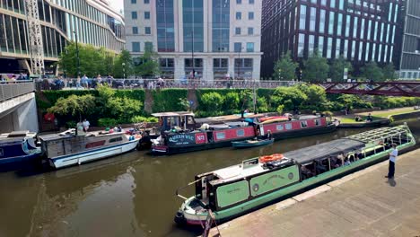 Daytime-footage-of-canal-boats-floating-on-Regent's-Canal-in-Kings-Cross,-London,-with-a-visible-pedestrian-area