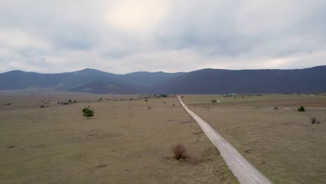 Ein-Wunderschönes-Landschafts-Drohnenvideo-Von-Einem-Leeren-Feld-Mit-Einer-Straße-In-Der-Kroatischen-Region-Lika-In-Europa