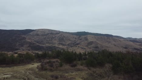 Perspectiva-Aérea-Del-Paisaje-Volcánico-De-Las-Montañas-De-Rumania-Con-Sus-Volcanes-De-Lodo,-Tierra-Seca-Con-Grietas,-Con-Algunas-Casas-Y-Pueblos-Aislados