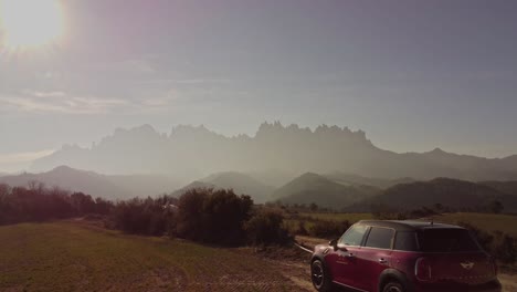 Red-SUV-parked-in-rural-Spain-with-Montserrat-mountains-in-the-background-at-sunrise