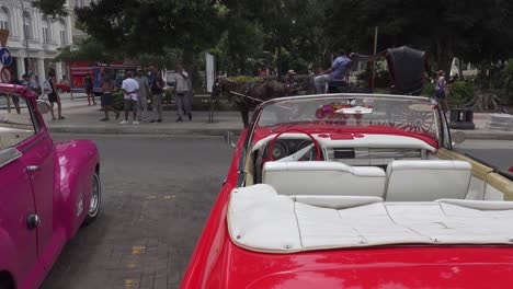 American-vintage-convertible-cars-from-19650s-and-1960s-at-Parque-Central-in-Havana,-Cuba,-panning-shot