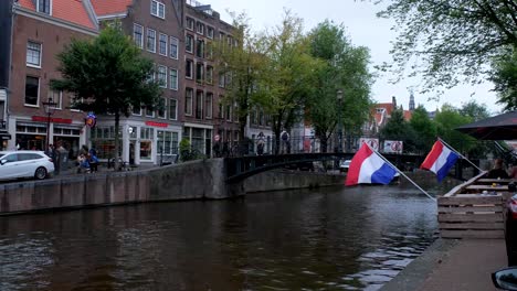 Barco-Clásico-En-El-Canal-De-Ámsterdam-Fluyendo-Hacia-El-Pintoresco-Puente-De-Hierro-Durante-El-Día.