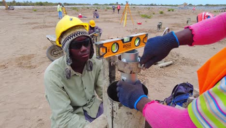 Técnicos-De-Construcción-Africanos-Nivelando,-Midiendo-Y-Ajustando-El-Molde-Del-Marco-De-Pilotes-De-Hormigón-Y-El-Soporte-Para-Pilotes-De-Hormigón-Solares-Fotovoltaicos.