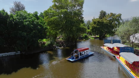 Drone-Siguiendo-Una-Trajinera-Flotando-Por-Los-Canales-Del-Lago-Xochimilco,-En-México