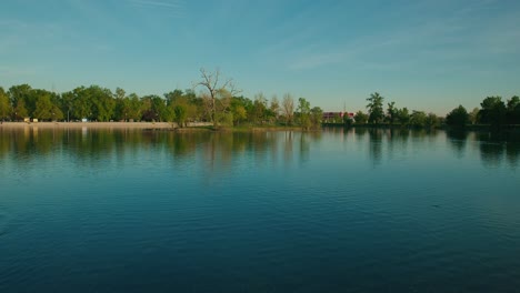 Wide-view-of-a-calm-lake-with-tree-reflections-and-a-clear-sky-at-Jarun-Lake,-Zagreb-Croatia