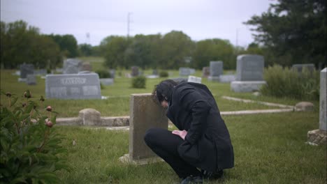 Man-mourning-over-death-of-loved-one-at-grave-tombstone-in-cemetery