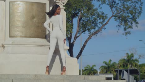 A-young-girl-in-a-white-bodysuit-revels-in-a-city-day-with-a-statue-behind-her