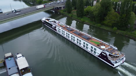 River-Cruise-Ship-on-the-Seine-Passing-Under-a-Bridge-AERIAL-BEHIND