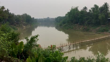 Buddhist-monk-crossing-bamboo-bridge-in-Luang-Prabang,-Laos