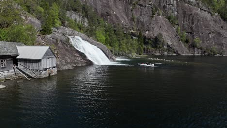 Tourists-on-guided-Norway-Fjord-Safari-driving-into-waterfall-with-their-boat,-aerial-approaching