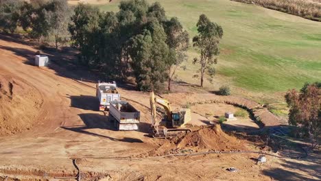 Yarrawonga,-Victoria,-Australia---29-May-2024:-Truck-and-trailer-moving-into-position-for-a-tracked-excavator-to-load-dirt-from-atop-a-dirt-pile