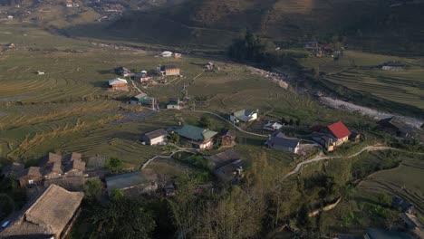 Aerial-drone-shot-of-villages-amidst-bright-green-rice-terraces-in-the-mountains-of-Sapa,-Vietnam