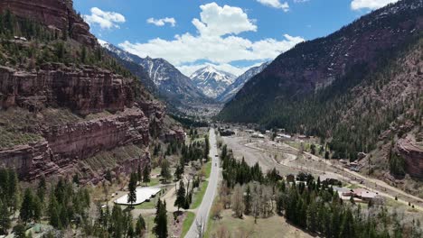 Vista-Aérea-De-La-Carretera-Con-Montañas-A-Ambos-Lados-Con-Un-Pico-Nevado-Al-Fondo,-Ouray-Colorado