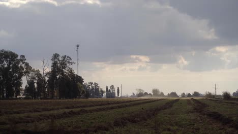 Handheld,-wide-view-of-a-plowed-field-with-distant-dust-produced-by-a-tractor-at-work-plowing-the-field