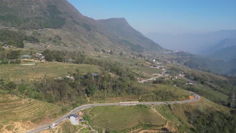 Aerial-drone-shot-of-road-winding-through-bright-green-rice-terraces-in-the-mountains-of-Sapa,-Vietnam