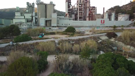 Fábrica-De-Cemento-Cerca-De-Costa-Garraf,-Barcelona-Con-Exuberante-Vegetación-En-Primer-Plano