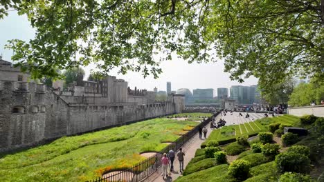 A-vibrant-daytime-scene-at-the-Tower-of-London,-Green-Moat-Garden,-visitors-leisurely-stroll-in-front-of-this-iconic-historical-site,-concept-of-living-history-and-cultural-exploration