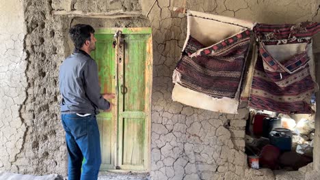 Un-Hombre-Está-Cerrando-Una-Puerta-Cerca-De-Madera-Antigua-Puerta-De-Ruina-Arcilla-Casa-De-Ladrillos-De-Barro-En-La-Cima-De-Una-Colina-Oasis-En-El-Desierto-Pueblo-De-Montaña-Campo-En-Marruecos-Rural-Gente-Local-Vida-Verano-Jardín-De-Palmeras-Datileras